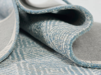 Blue and light gray woven rug with a subtle geometric pattern; soft textured pile and curled edge.