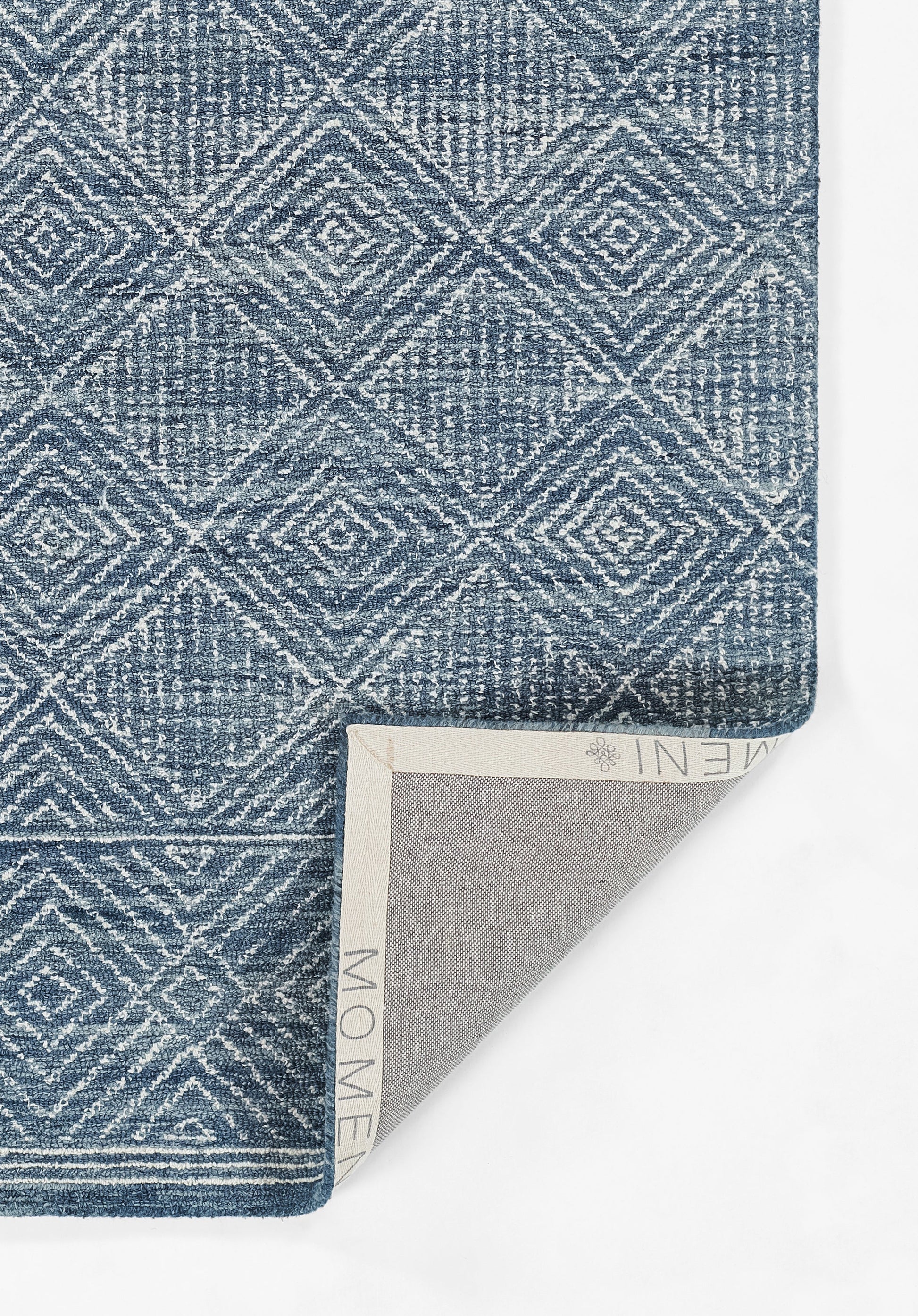 Muted blue geometric diamond rug with white lines, textured weave; folded corner reveals beige backing.