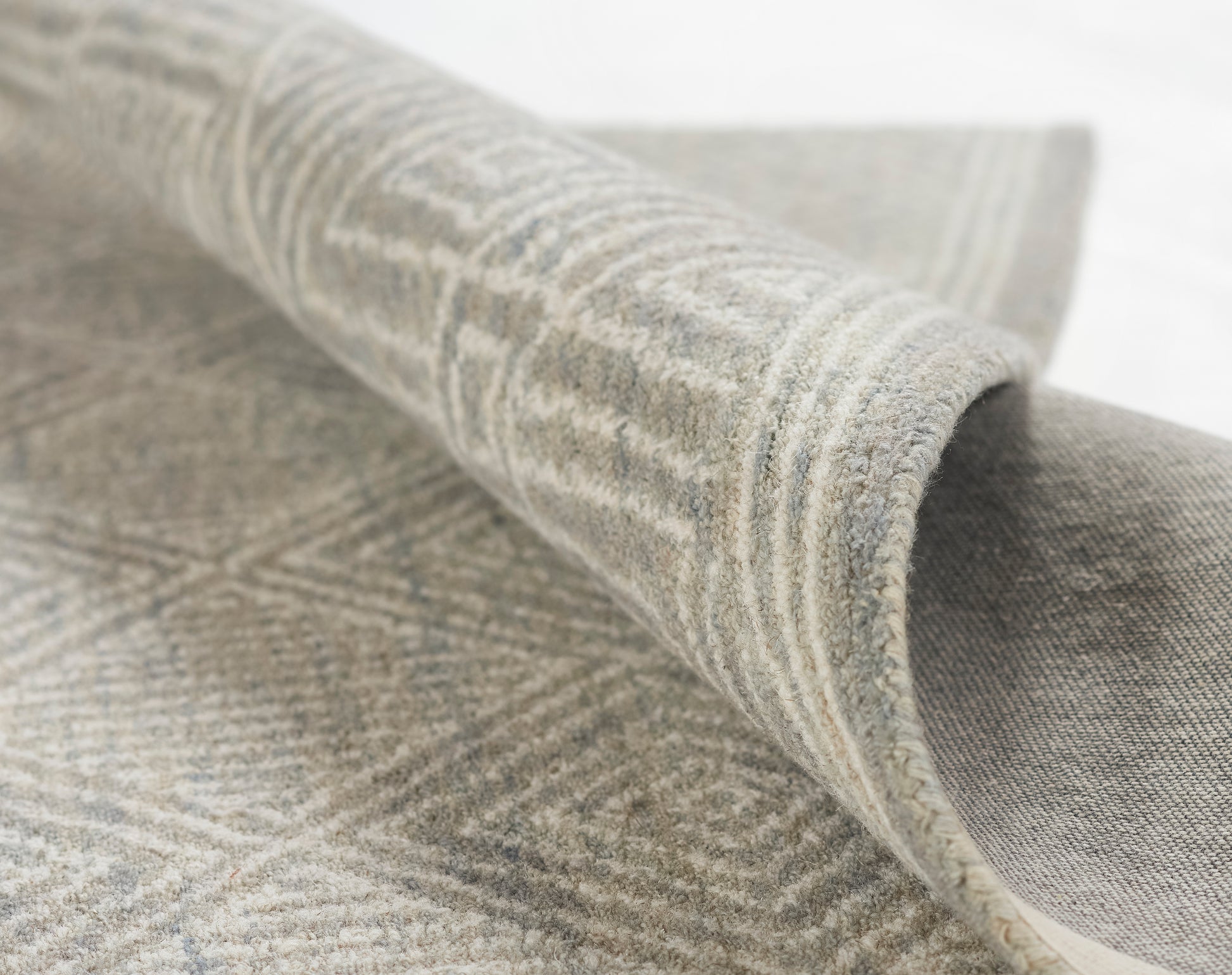 Grey and beige geometric rug with soft pile, rolled edge showing woven texture.