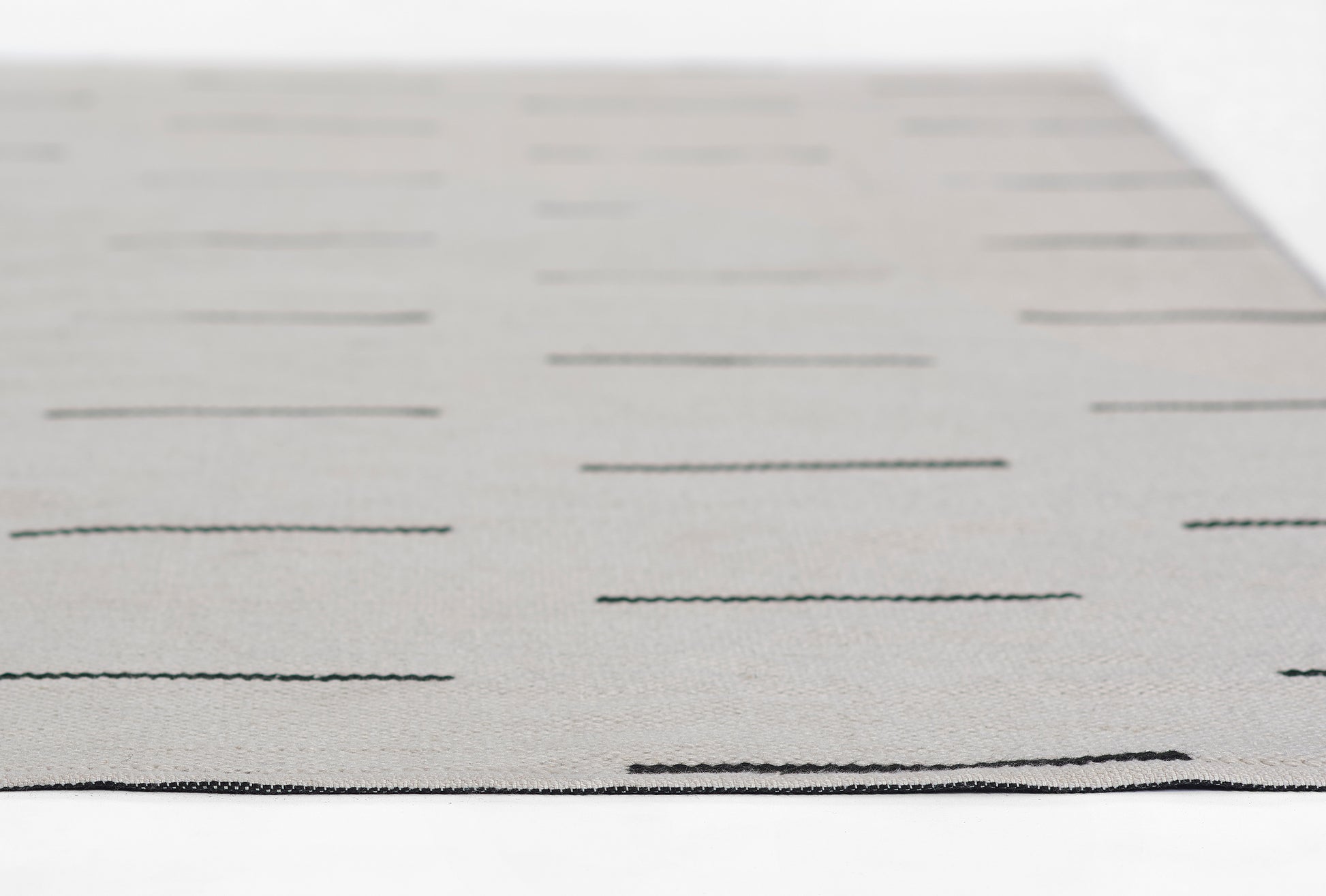 Gray flat-weave rug with subtle dark horizontal dash lines, rectangular modern decor piece.