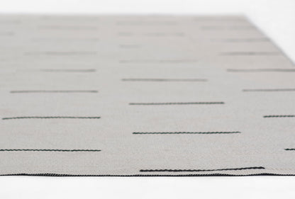 Gray flat-weave rug with subtle dark horizontal dash lines, rectangular modern decor piece.