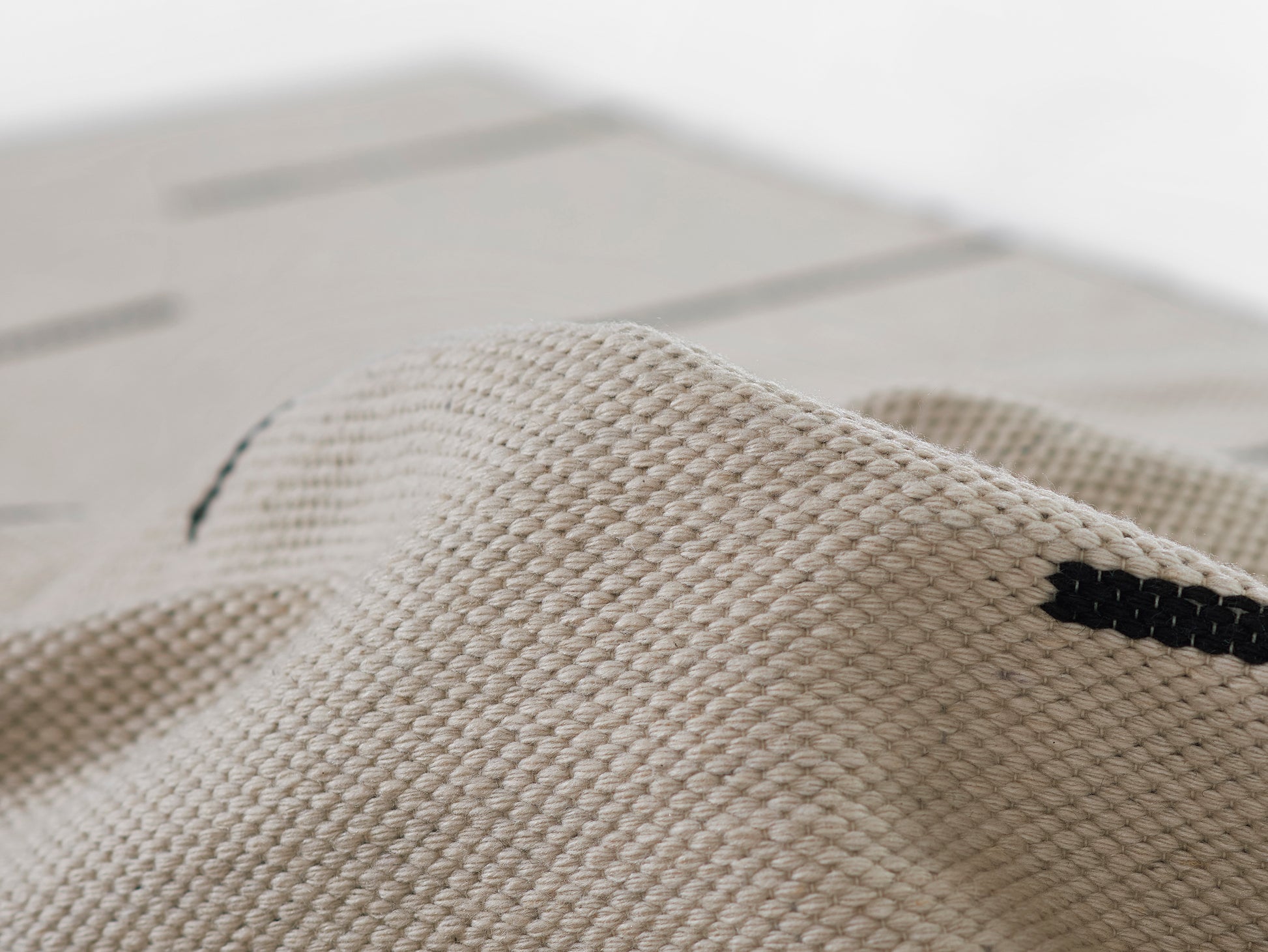 Beige woven rug close-up with a thick texture and a black stripe, draped on a light wooden surface.