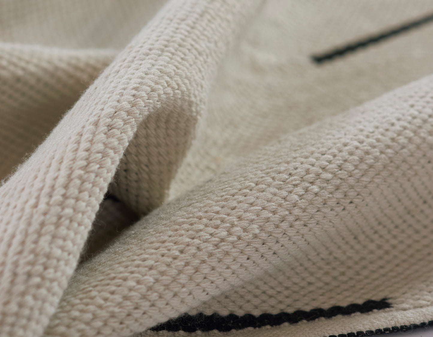 Ivory knitted rug with chunky texture and a dark navy stripe.