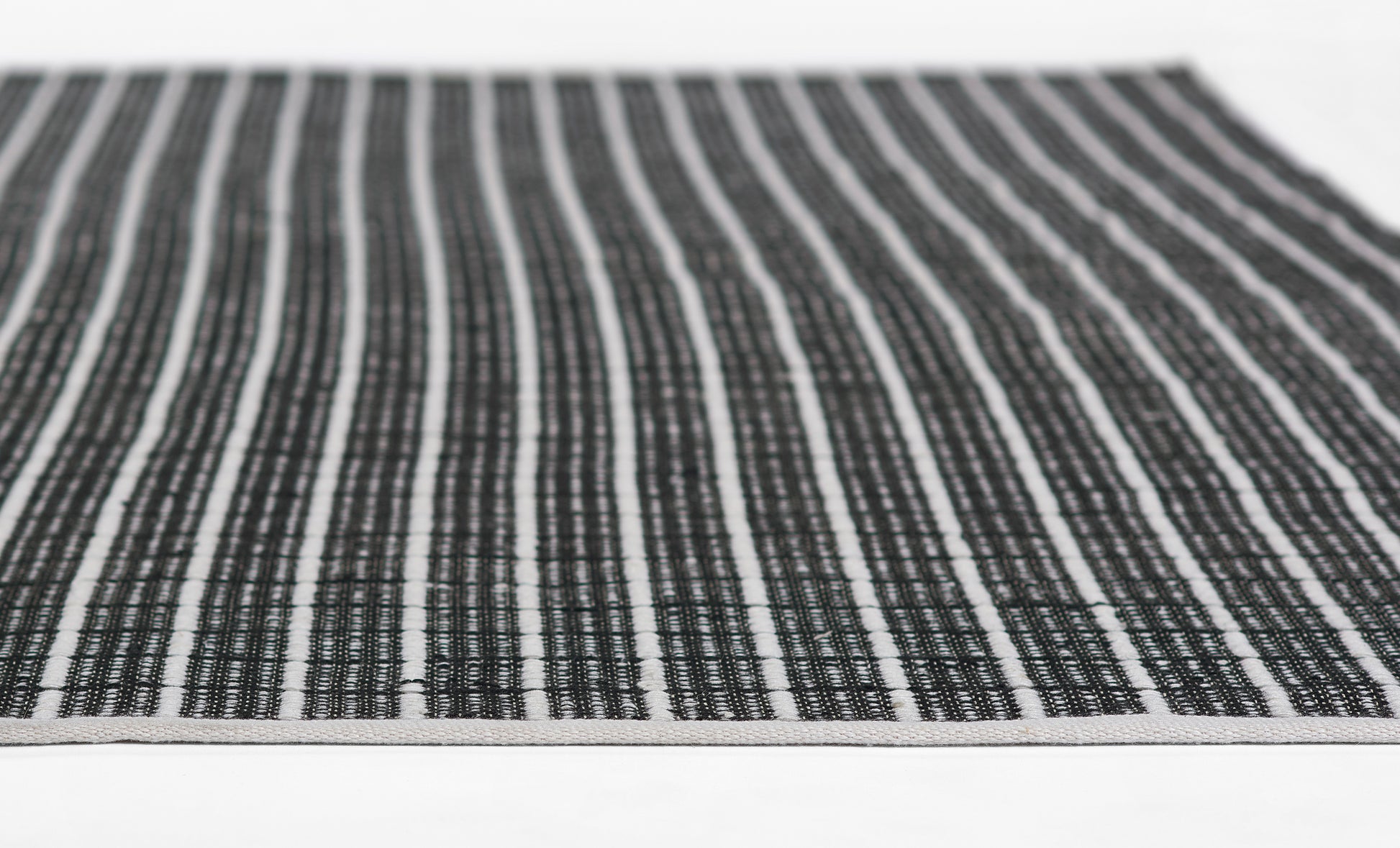 Rectangular black-and-white striped woven rug with a textured cotton-like surface; minimalist casual decor.