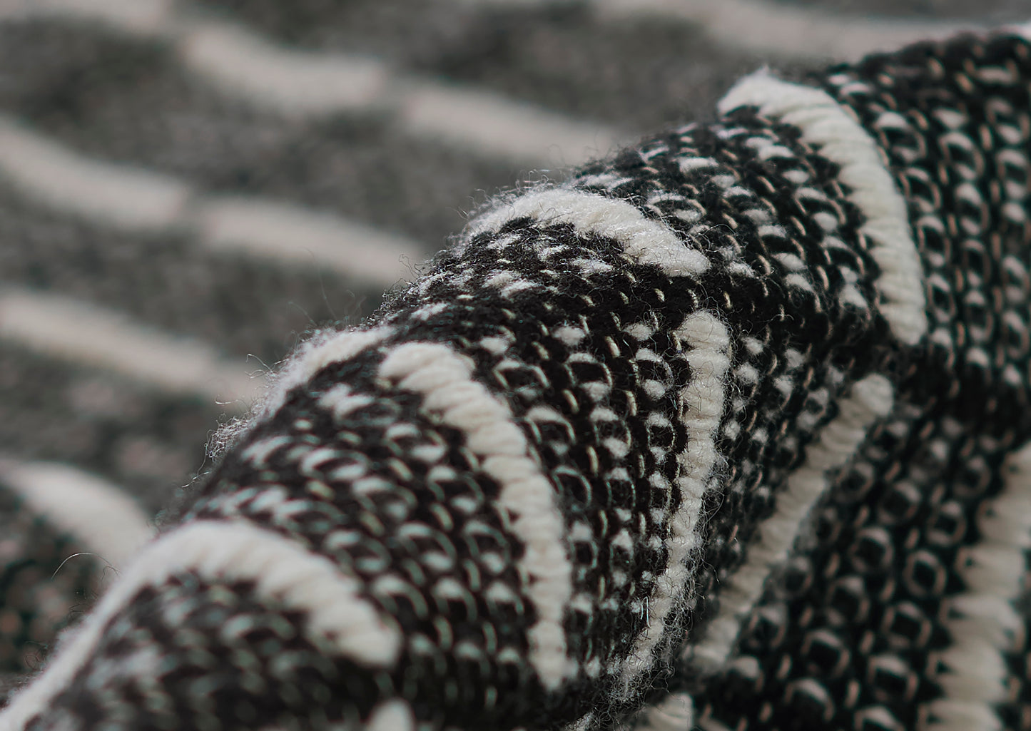 Close-up of black & white boucle textile rug with striped pattern and looped weave, rolled edge.