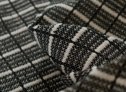 Close-up of black and white woven rug with boucle texture and plaid-like pattern.