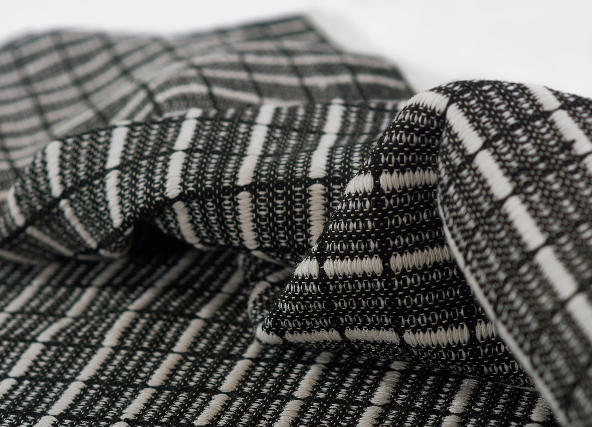 Close-up of black and white woven rug with geometric striped pattern, folded to show texture.