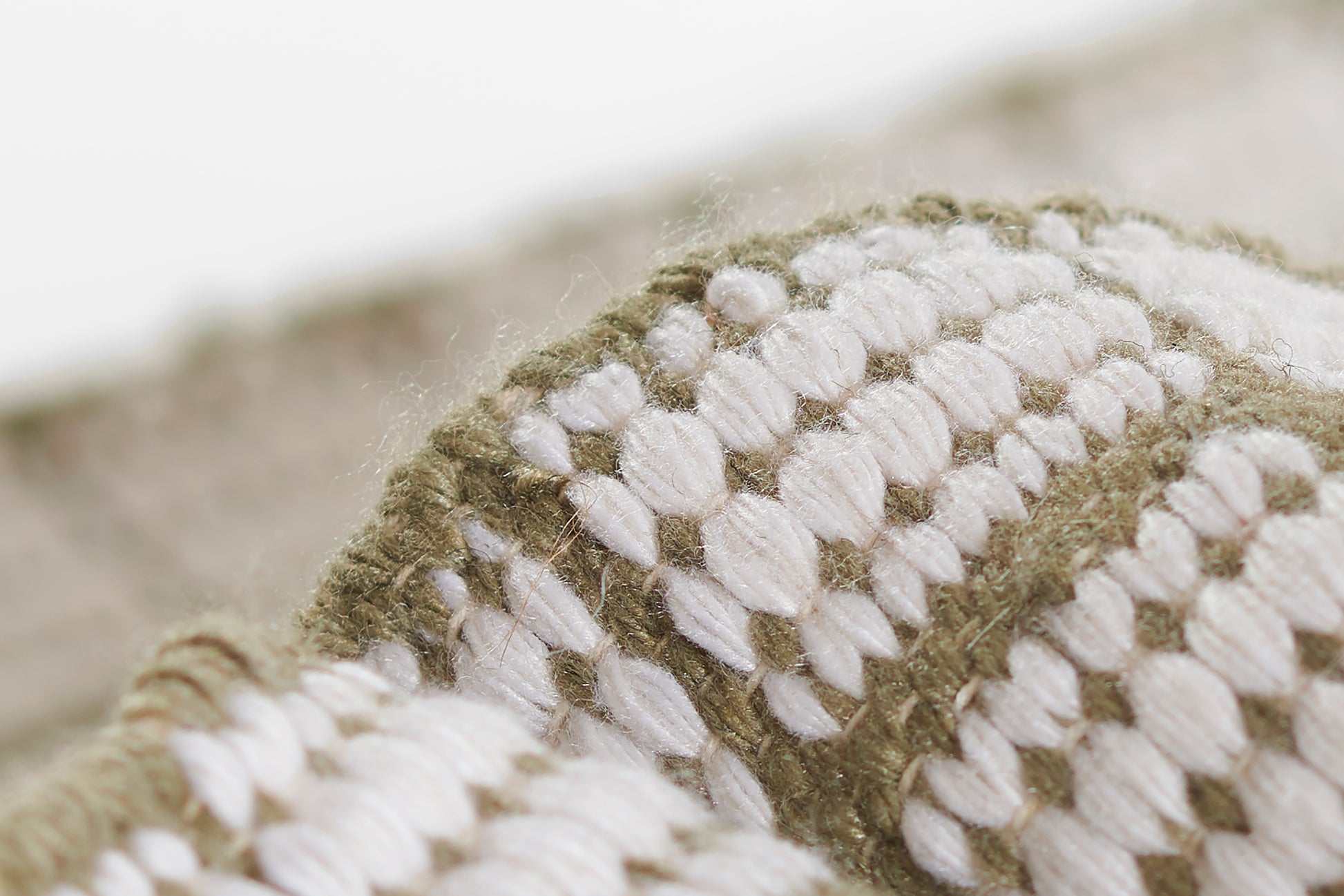 Close-up of a chunky wool runner with olive green and white stripes and a thick woven texture.