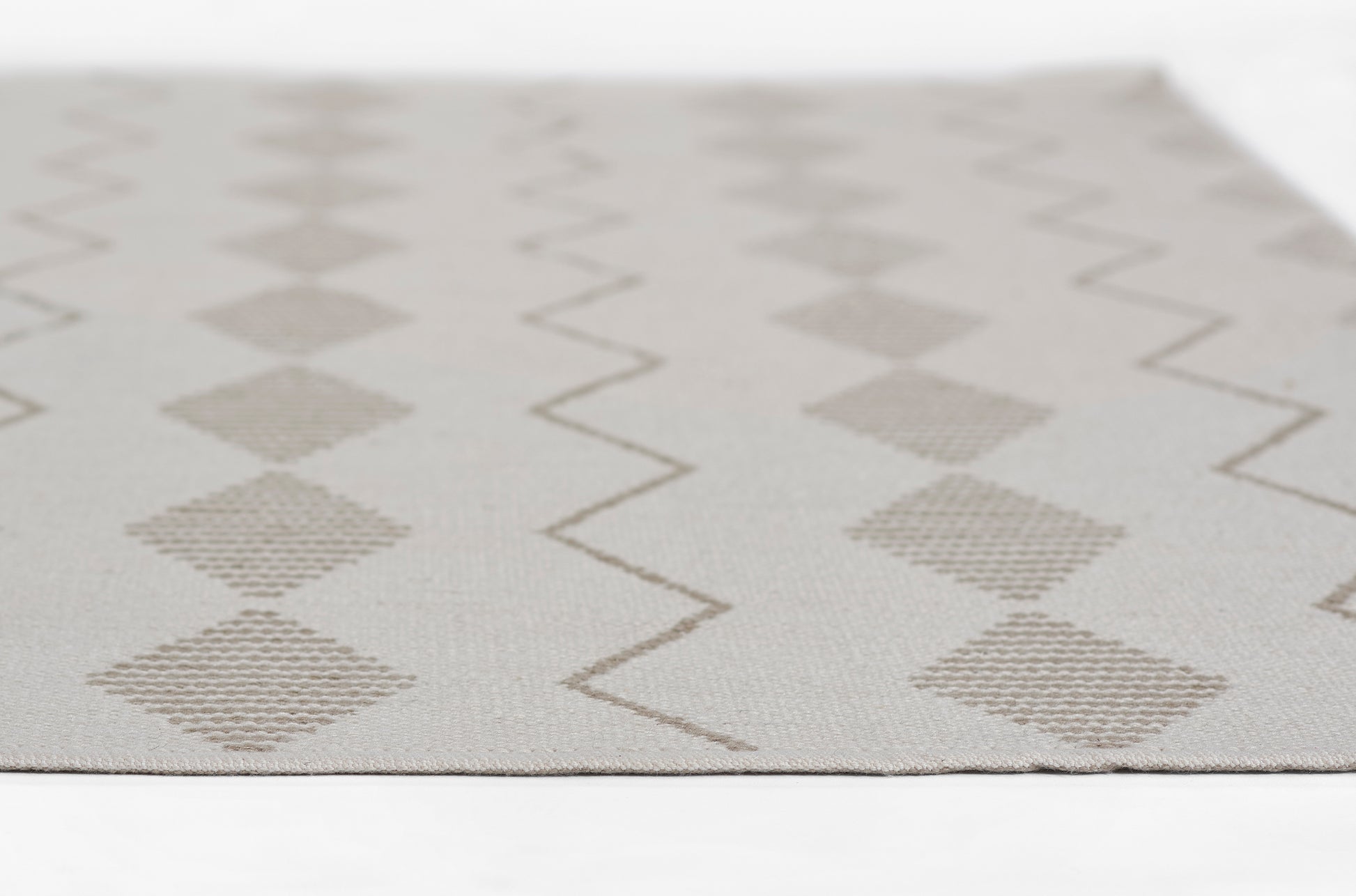 Beige woven rug with geometric diamonds and zigzag lines on ivory background.