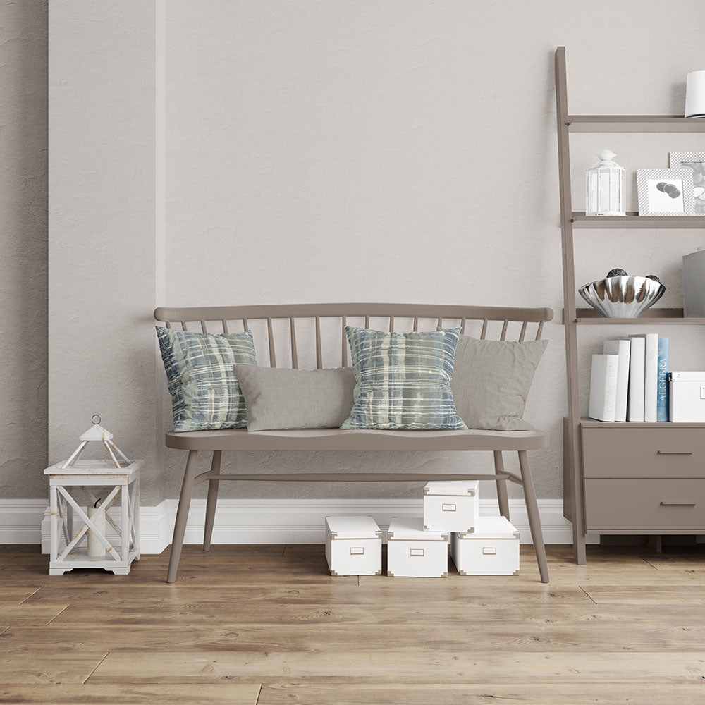 Taupe wooden bench with slat back and four cushions (two striped teal, two solid gray) in a living room with shelving.