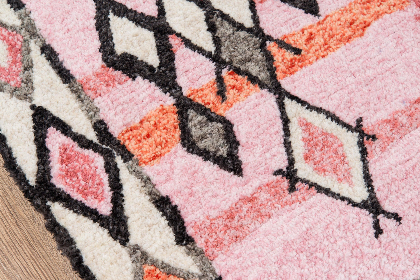 Pink shag rug with cream, orange and black geometric diamond patterns and plush pile.