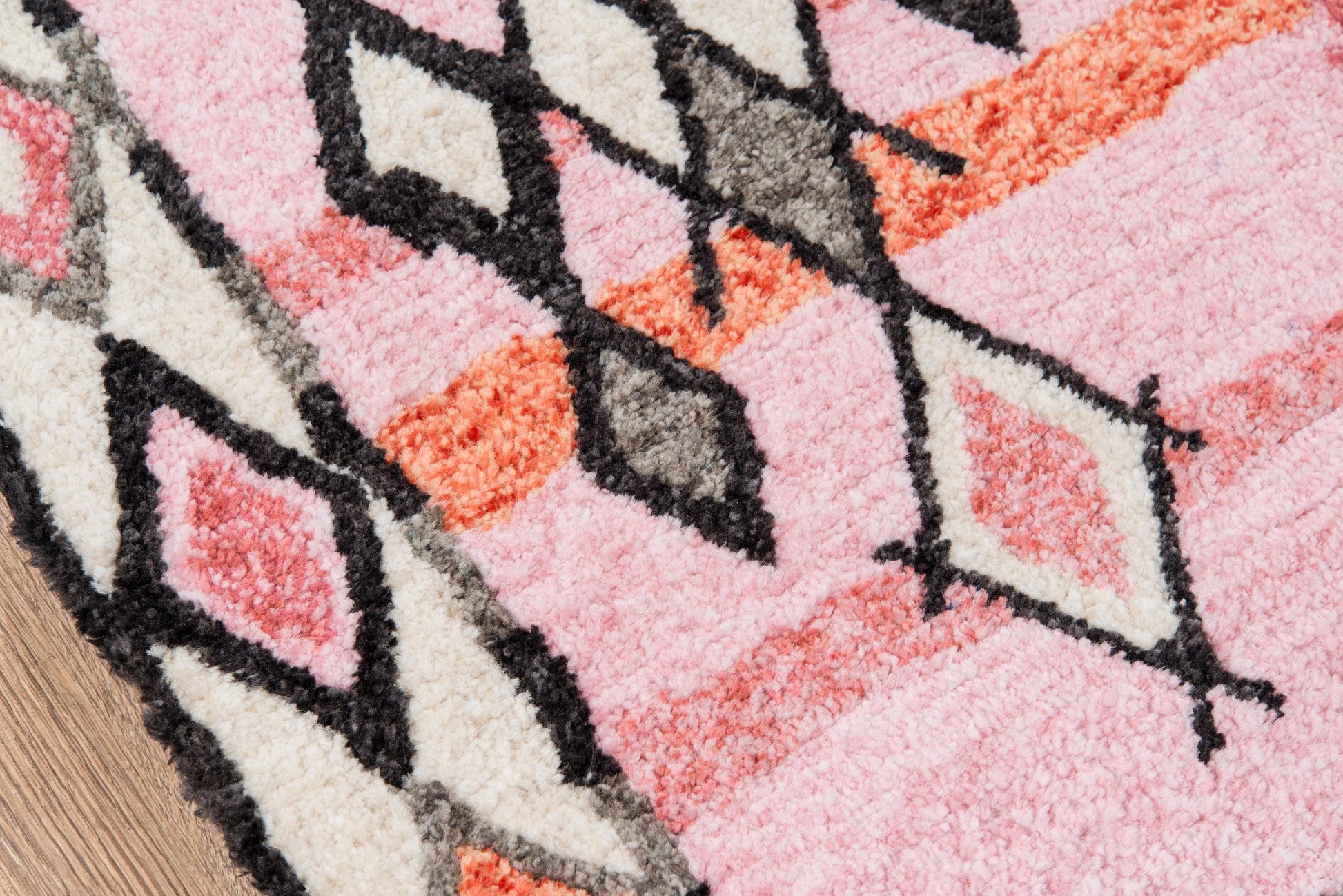 Pink shag rug with cream, orange and black geometric diamond patterns and plush pile.