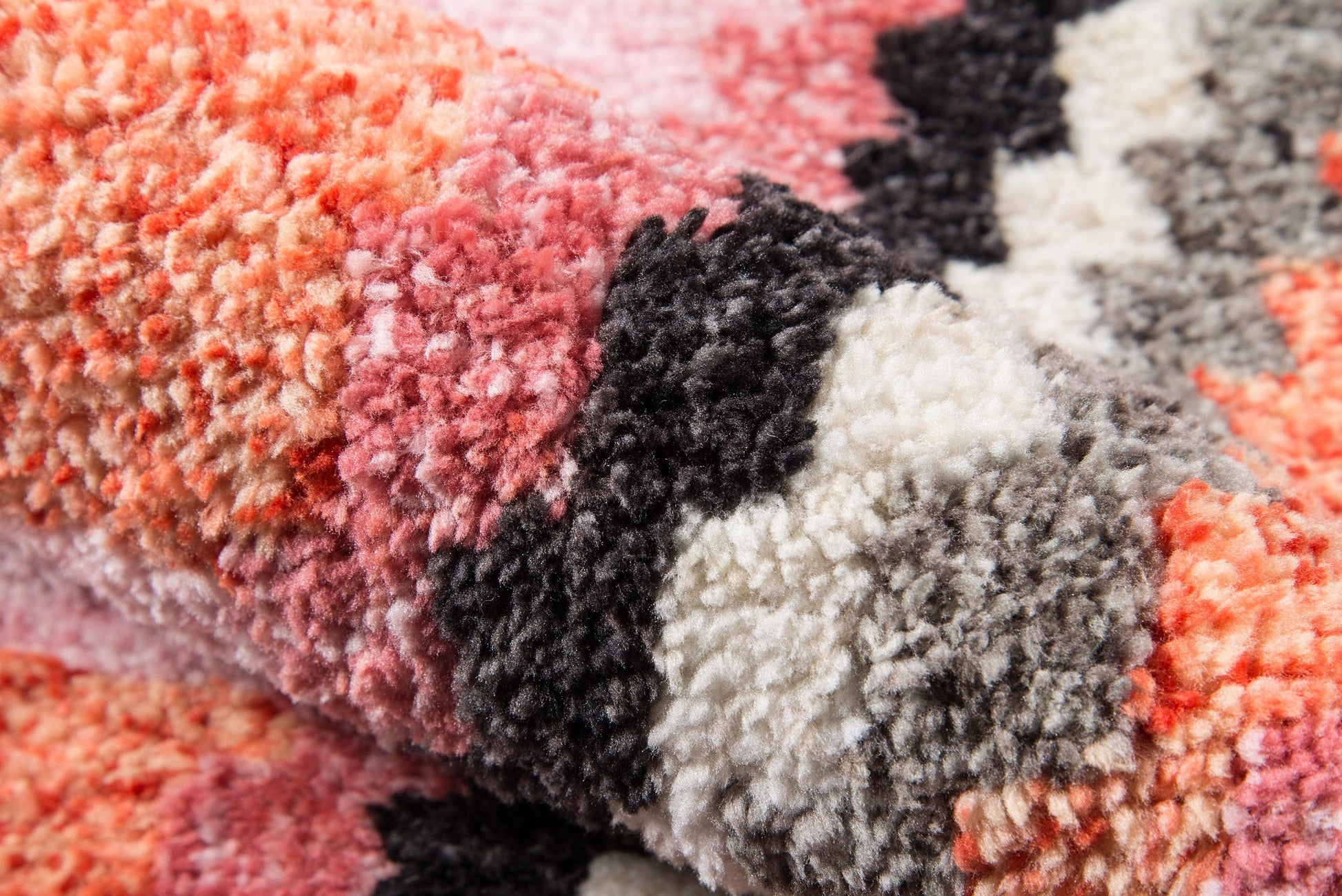 Close-up of a multicolor shag rug: pinks, peaches, grays, black and ivory color blocks, soft high-pile plush.