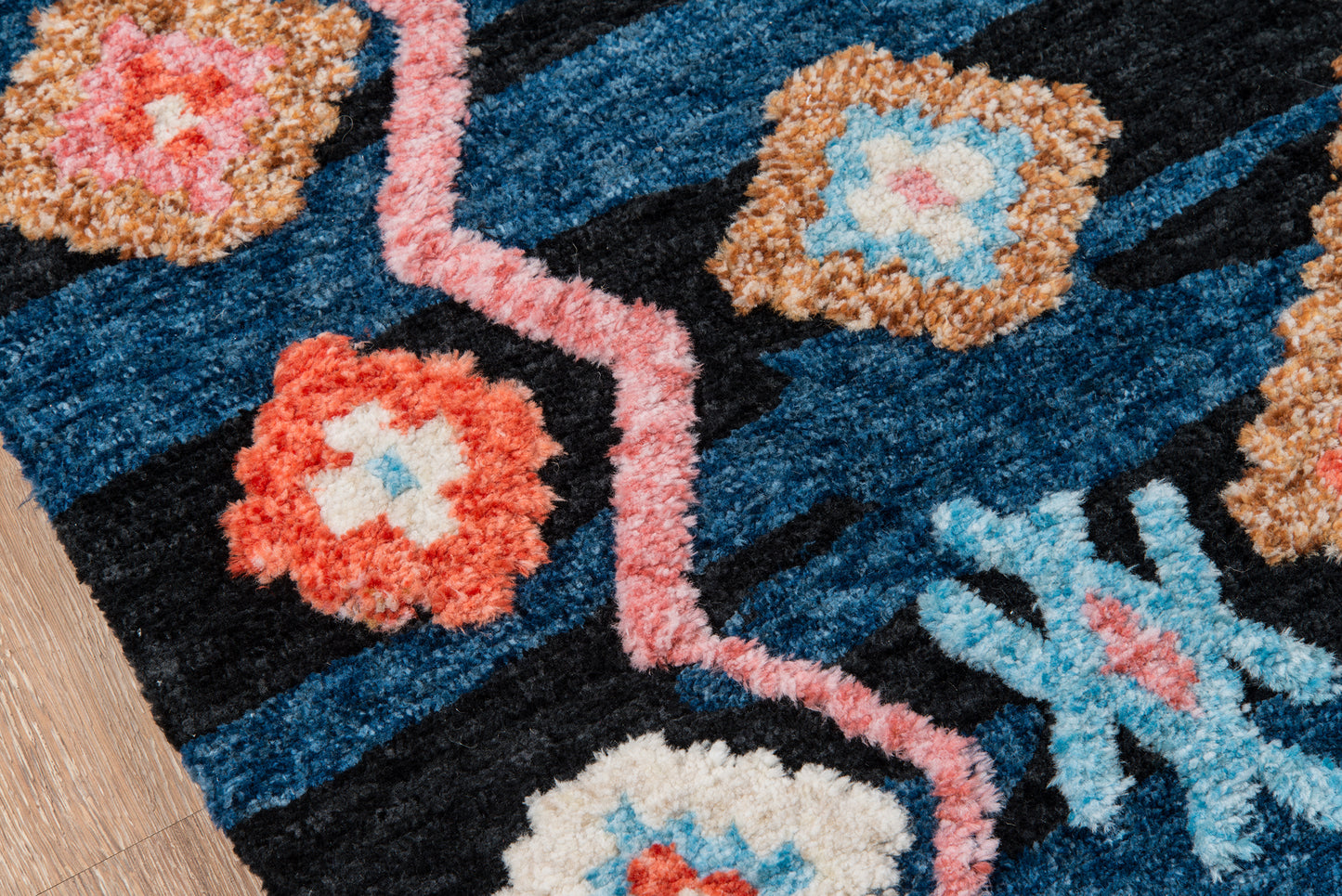 Navy blue patterned area rug with coral and sky blue floral motifs and pink zigzag border on wooden floor.