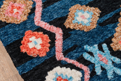 Navy blue patterned area rug with coral and sky blue floral motifs and pink zigzag border on wooden floor.