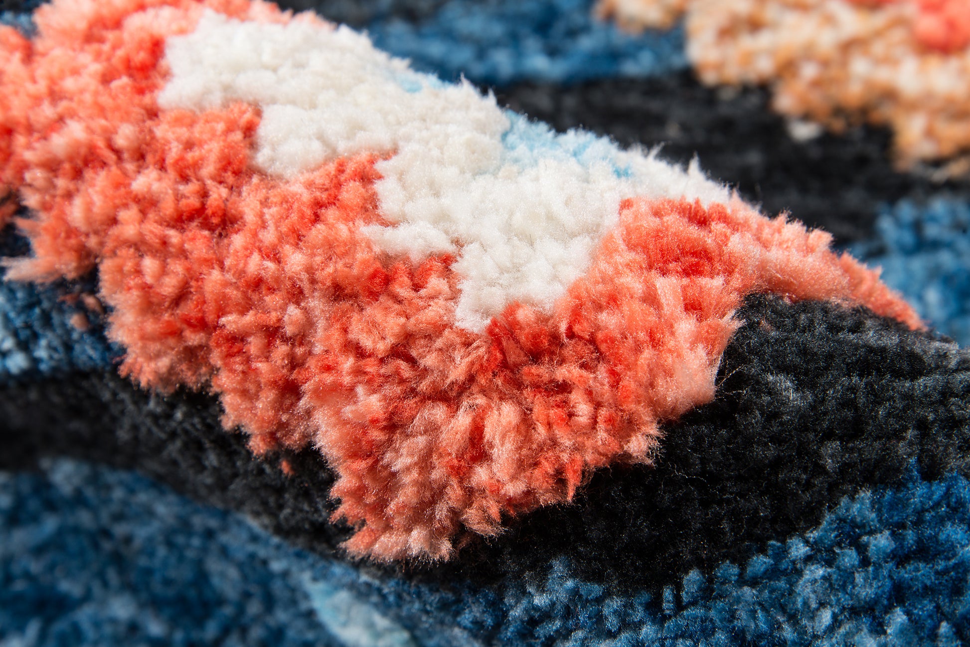 Close-up of a multicolor shag rug with coral pink, white, blue and black plush fibers.