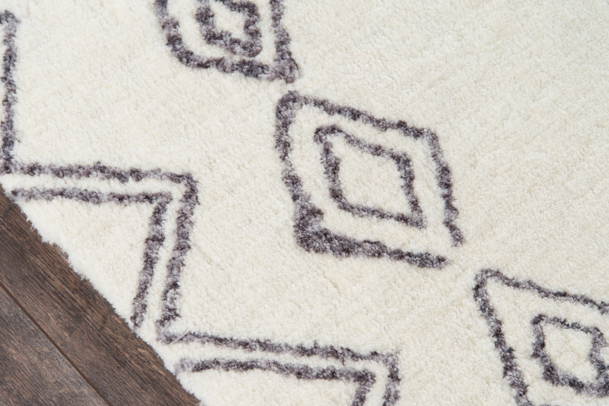 Cream shag rug with charcoal geometric diamond motifs on dark wood floor, plush pile