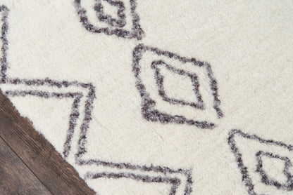 Cream shag rug with charcoal geometric diamond motifs on dark wood floor, plush pile