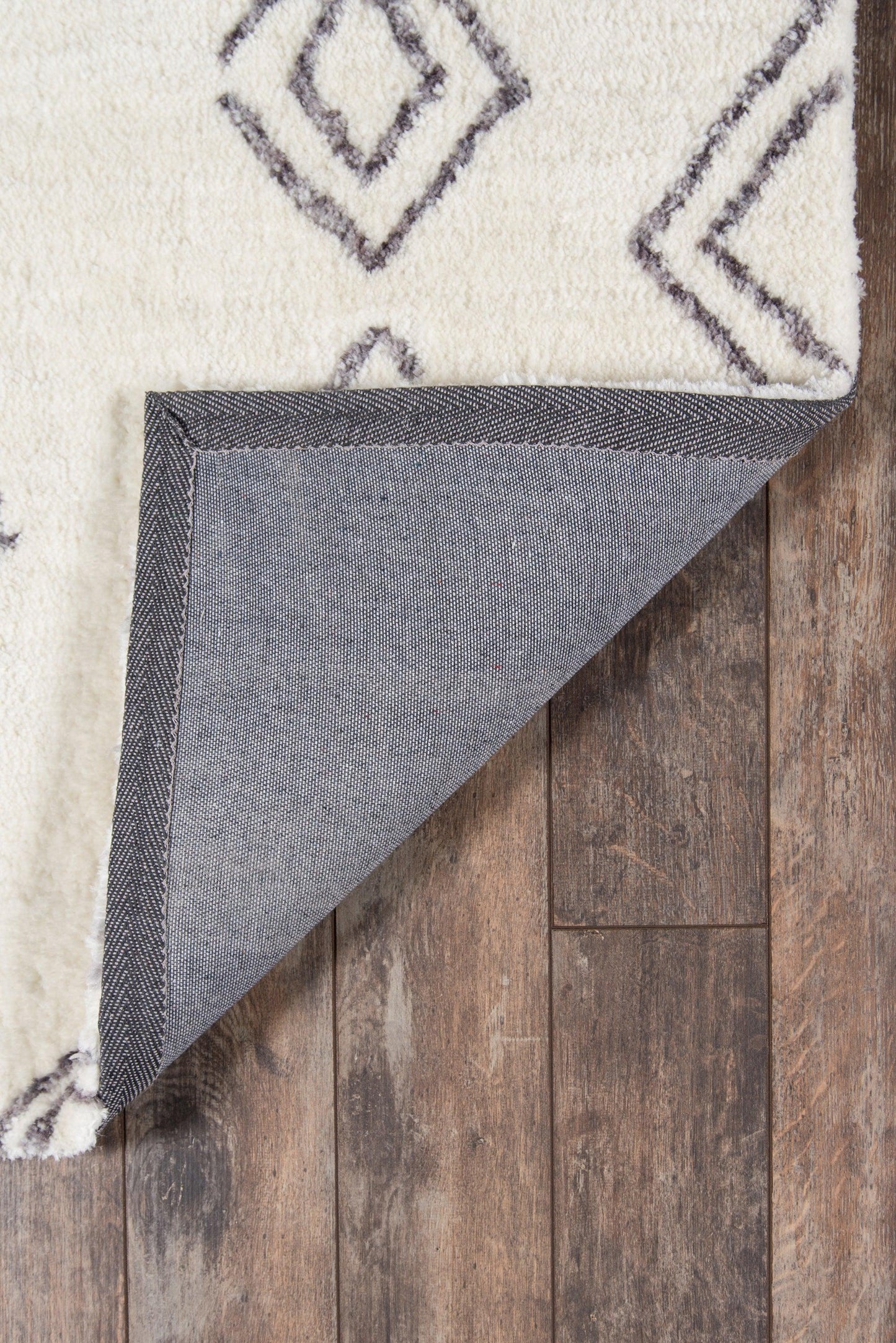 Ivory shag rug with purple diamond geometric pattern; folded corner reveals gray denim-like backing.
