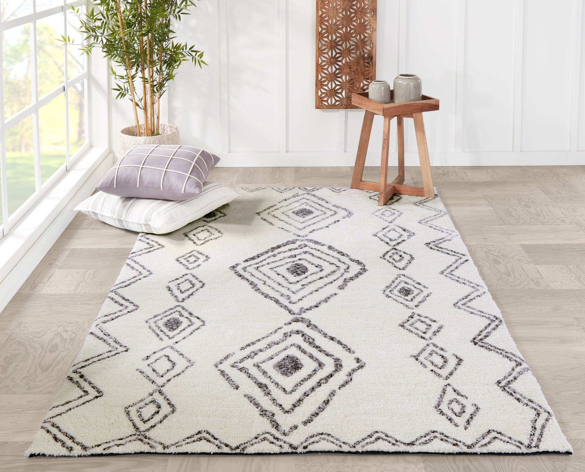 Ivory rug runner with gray diamond pattern and zigzag border; cushions, potted bamboo, and wooden side table in bright room.