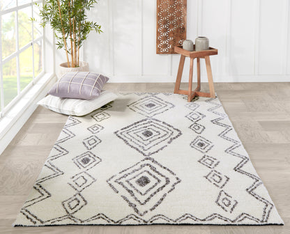 Ivory rug runner with gray diamond pattern and zigzag border; cushions, potted bamboo, and wooden side table in bright room.