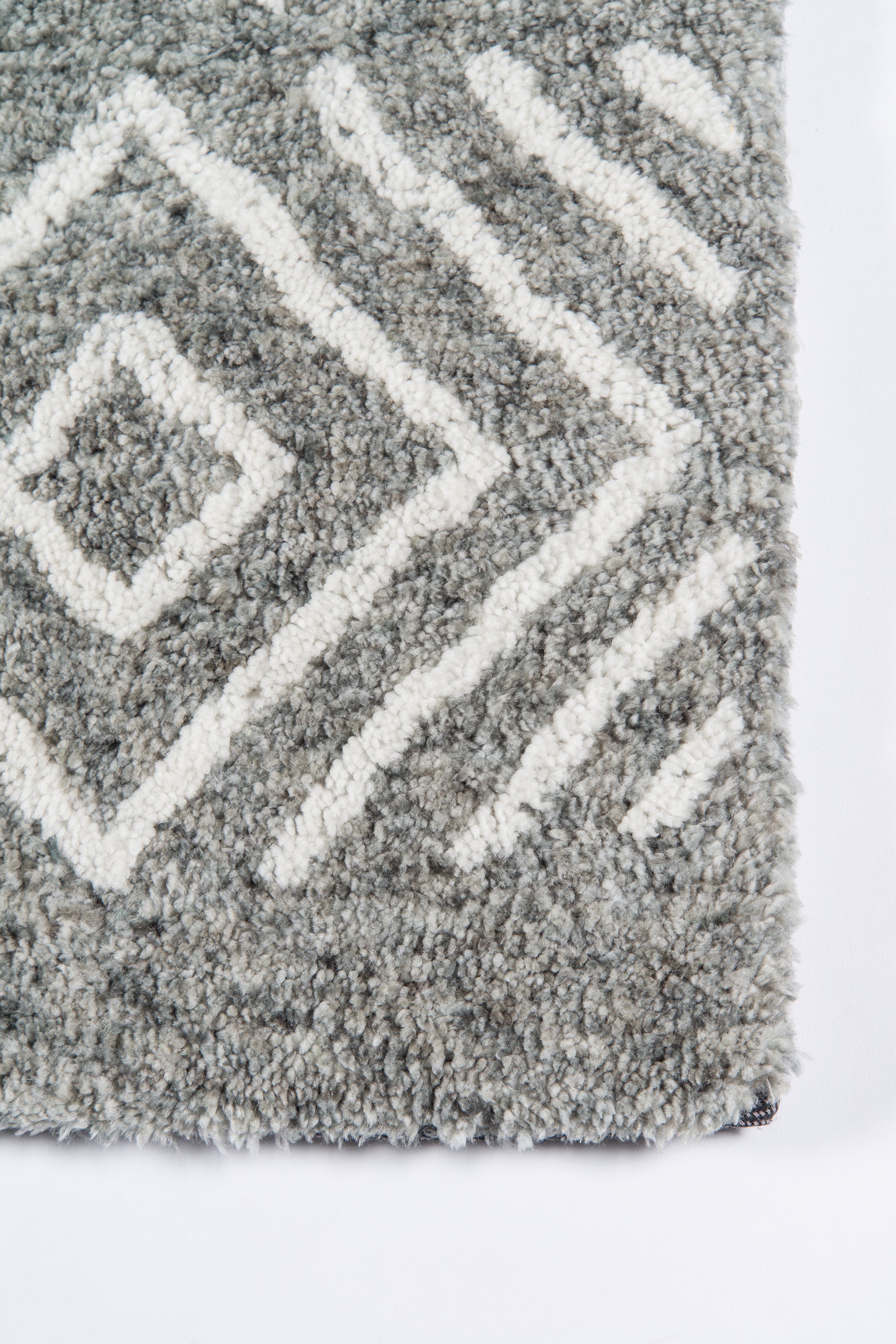 Grey shag rug with white diamond chevron pattern, plush thick pile, close-up of corner edge.