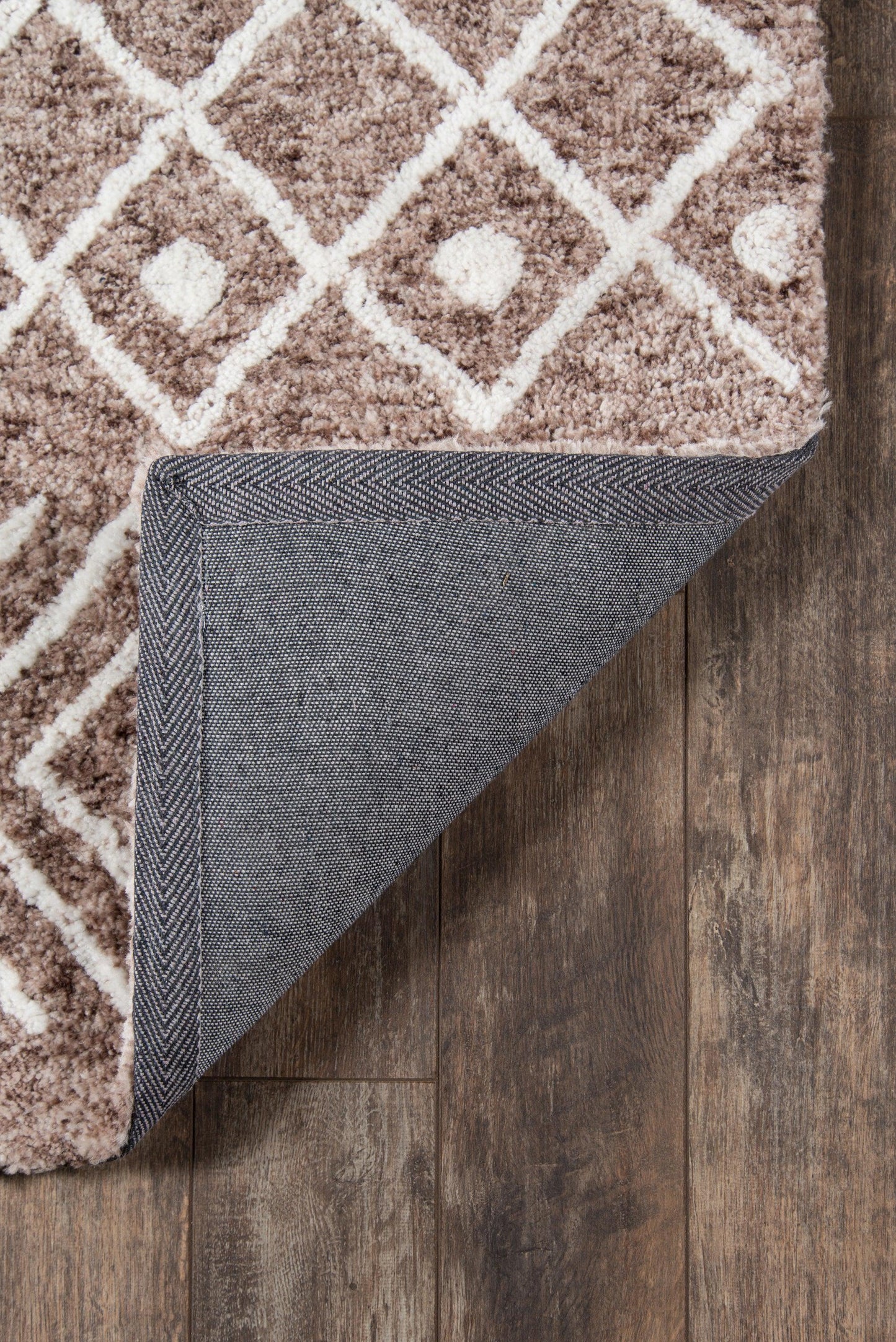 Brown shag rug with white geometric lattice pattern; folded corner reveals denim-gray backing on wood floor.
