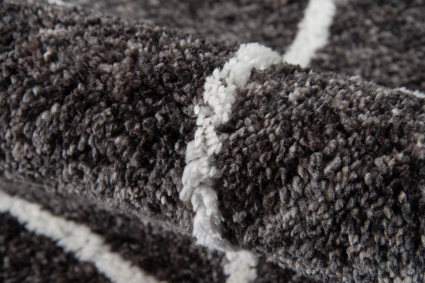 Close-up of dark gray shag rug with white geometric stripes, plush pile and textured fibers.