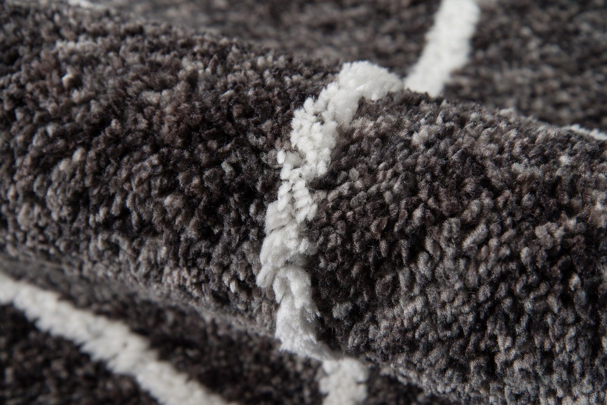Close-up of dark gray shag rug with white geometric stripes, plush pile and textured fibers.