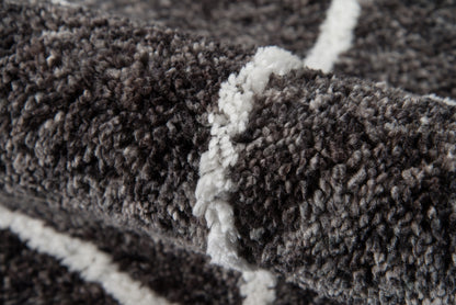 Close-up of dark gray shag rug with white geometric stripes, plush pile and textured fibers.