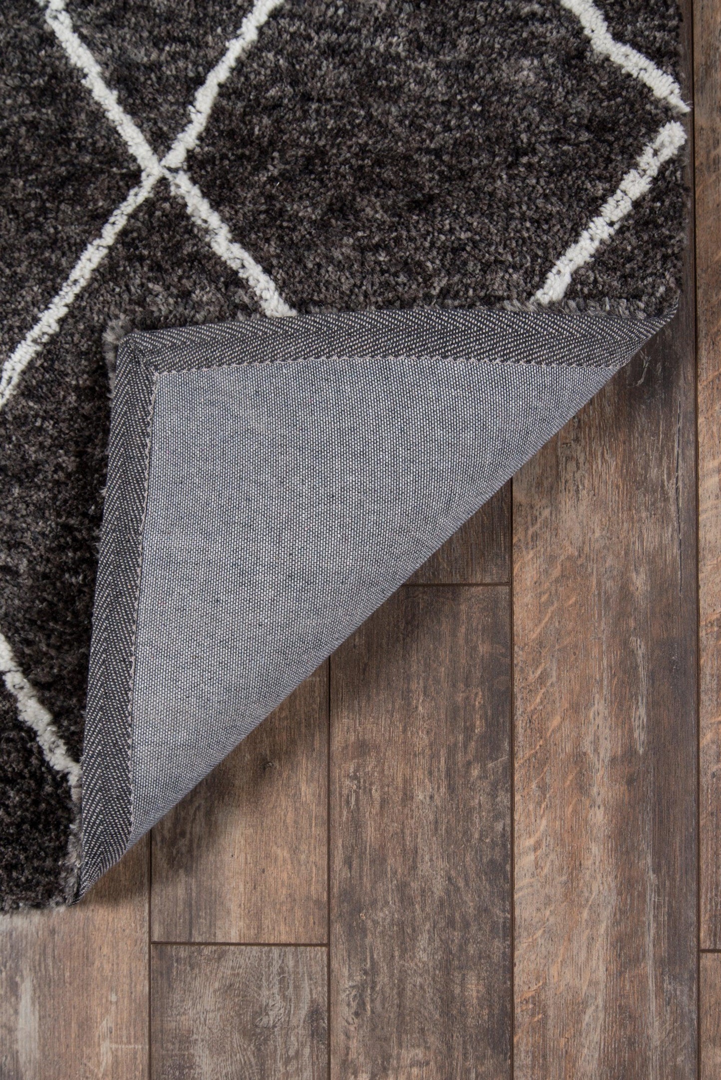 Charcoal shag rug with off-white geometric lattice pattern; folded corner shows grey backing on wooden floor.