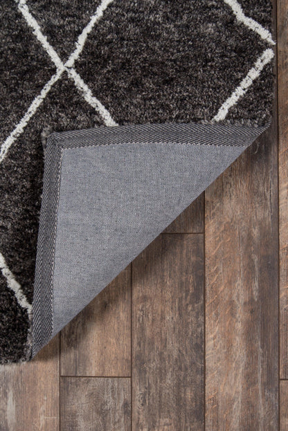 Charcoal shag rug with off-white geometric lattice pattern; folded corner shows grey backing on wooden floor.