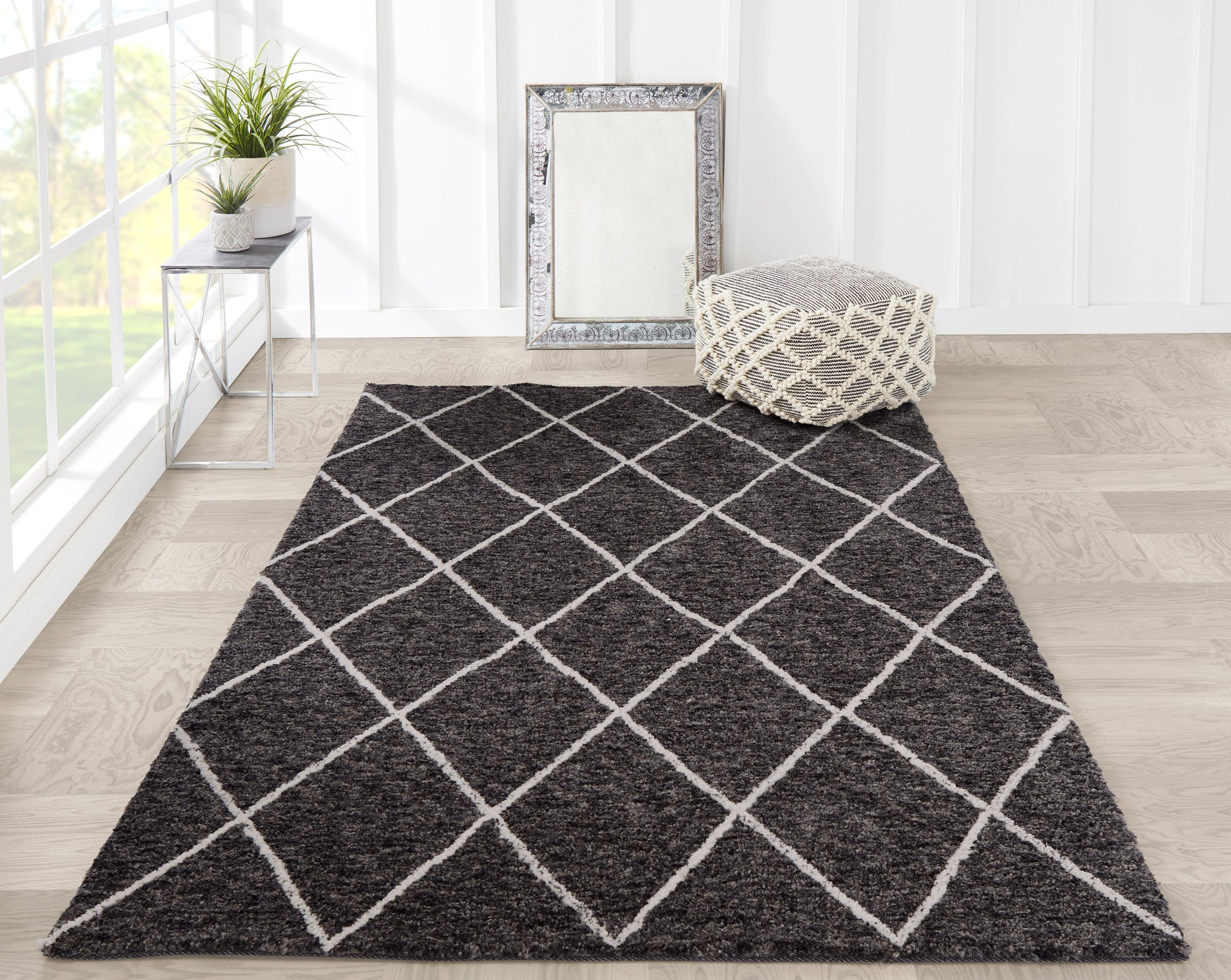 Plush dark gray rug with white diamond lattice, pouf, framed mirror, and plant on metal side table in bright sunlit room.