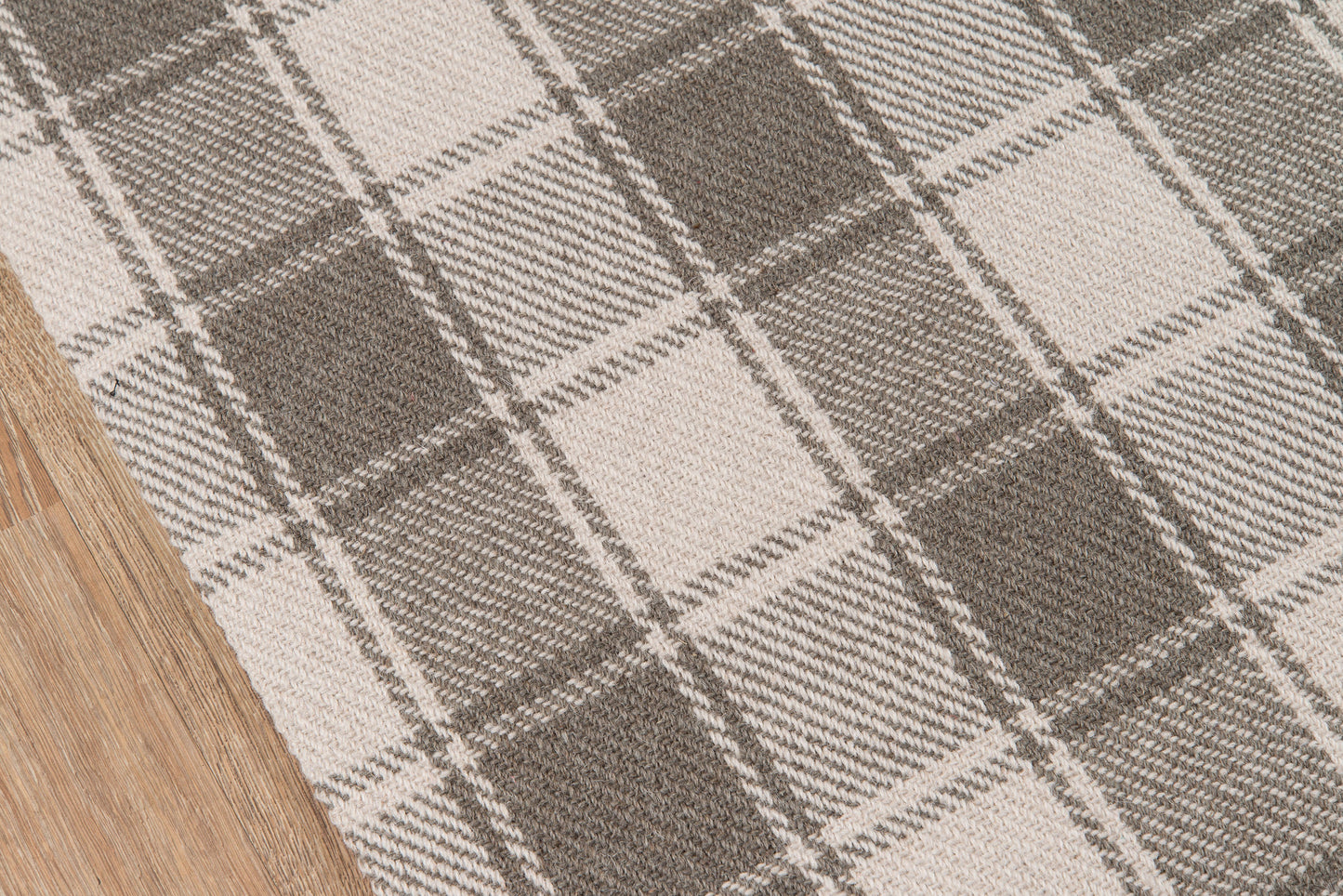 Woven plaid rug in beige and gray tones on wood floor; textured, chunky checkered pattern.