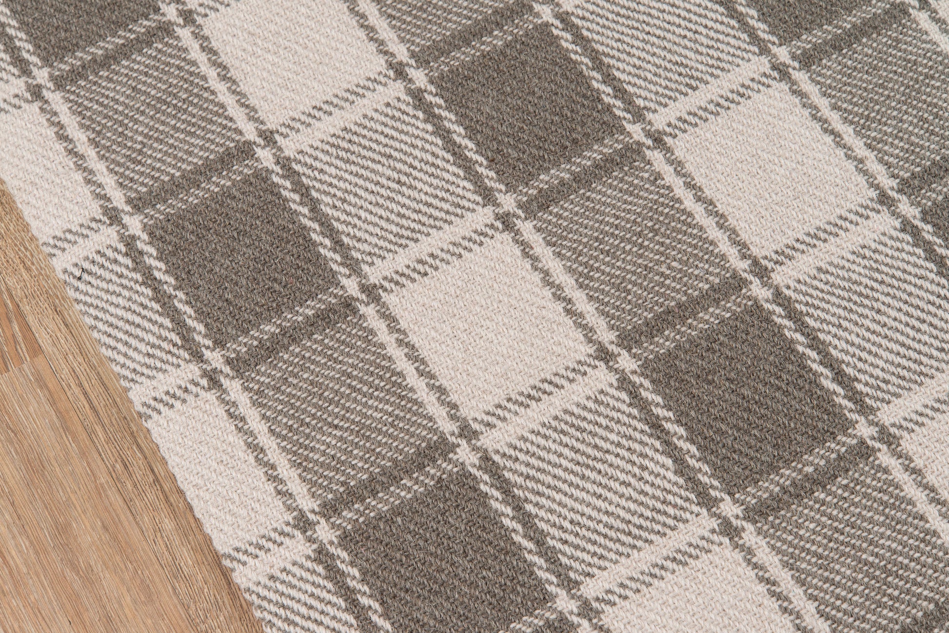 Beige and gray plaid rug with chunky woven texture on wooden floor.