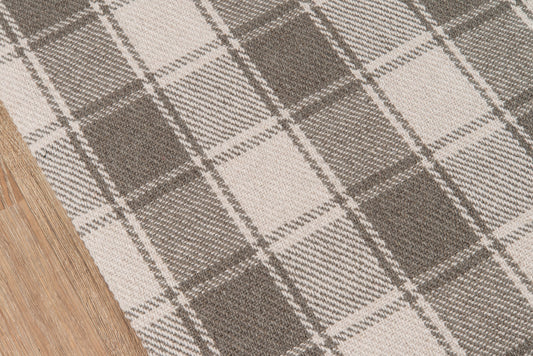 Gray & beige plaid rug with large taupe squares on a wooden floor; textured woven fabric.