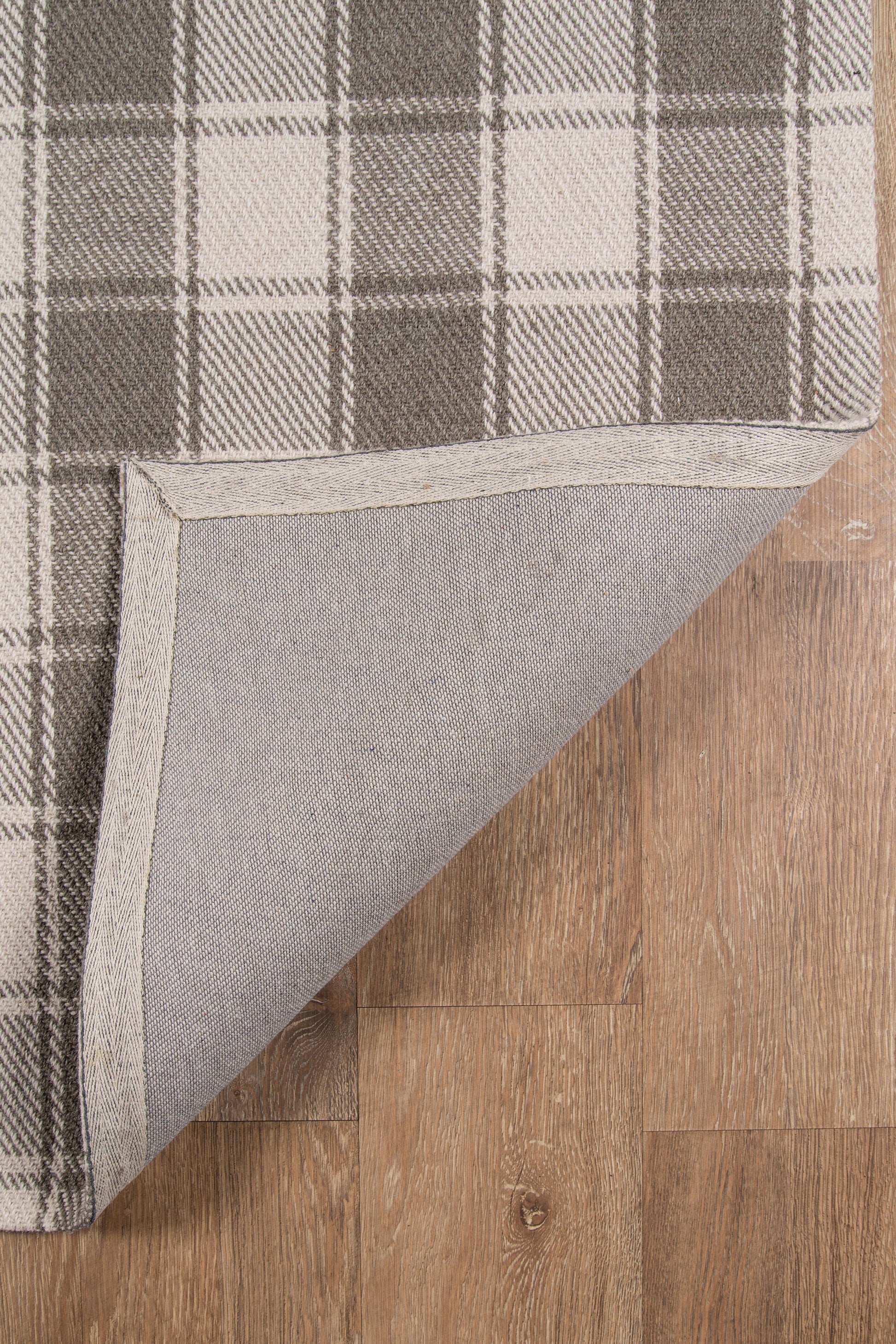 Grey plaid area rug with folded corner, light gray backing on wood floor.