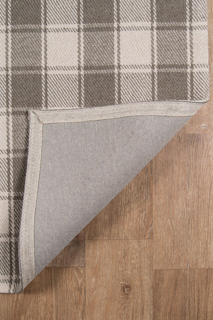 Grey plaid area rug with folded corner, light gray backing on wood floor.