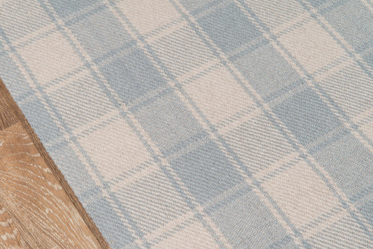Blue and beige plaid woven rug on light wood floor.