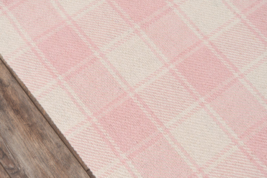 Pink and cream plaid woven rug on wooden floor; cozy, rustic home decor.
