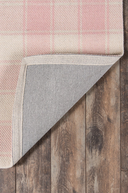 Rectangular pink plaid rug with beige border, woven texture, corner folded to reveal grey backing on wooden floor.