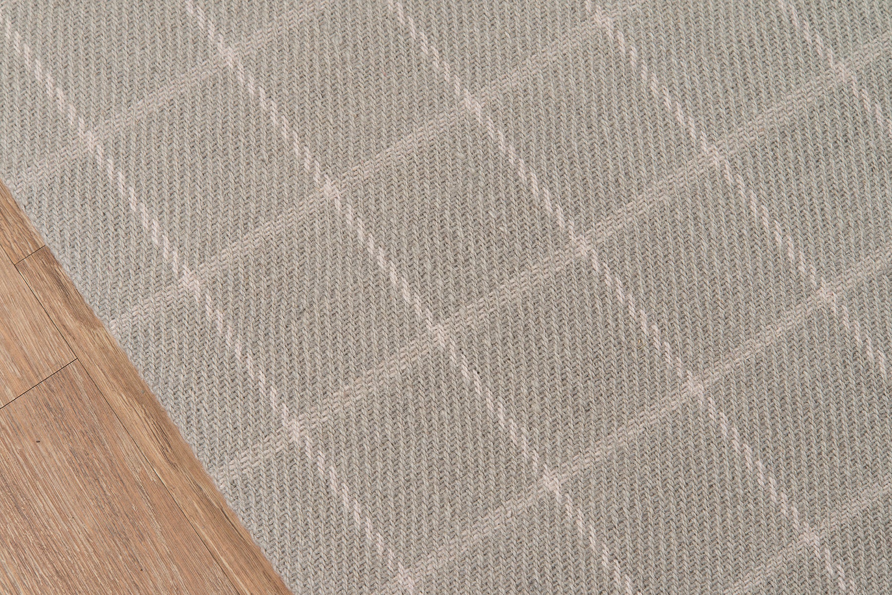 Gray plaid rug with large diamond pattern and textured weave on a wooden floor.