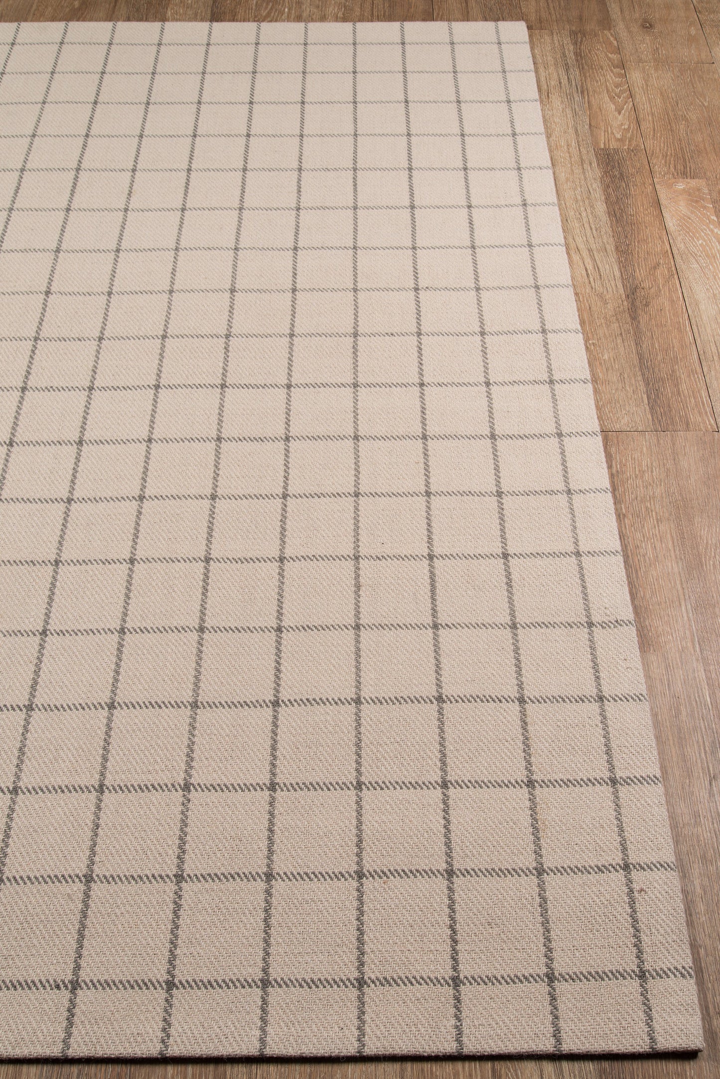 Beige rectangular rug with a dark gray square-grid pattern on a wooden floor.