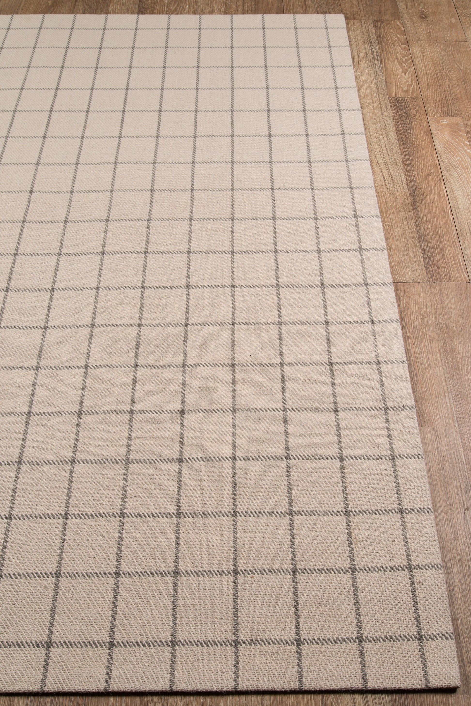Beige rectangular rug with a dark gray square-grid pattern on a wooden floor.