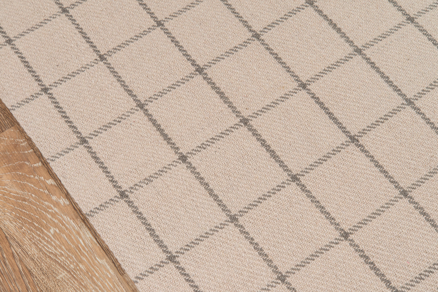 Beige woven rug with gray grid pattern beside a wooden floor.