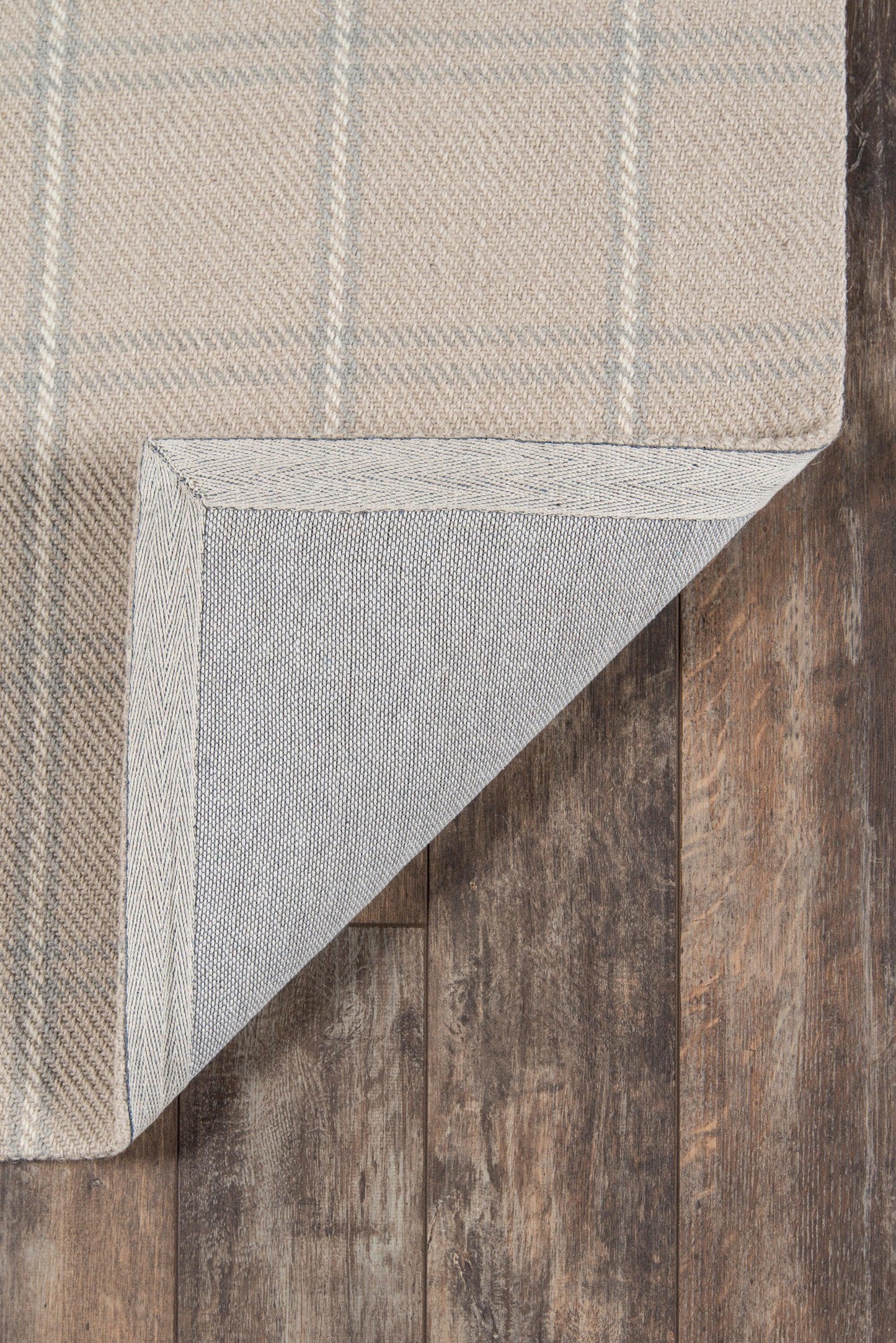 Beige plaid rug with pale blue stripes, folded corner reveals underside on dark wood floor.