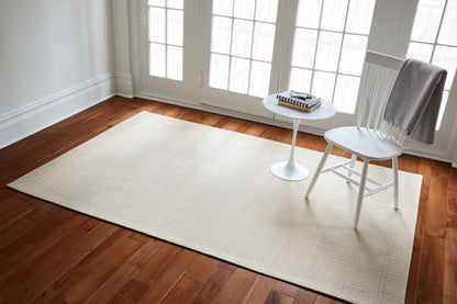 Beige striped rug on hardwood floor beside a white chair and round marble-topped side table; soft gray throw.