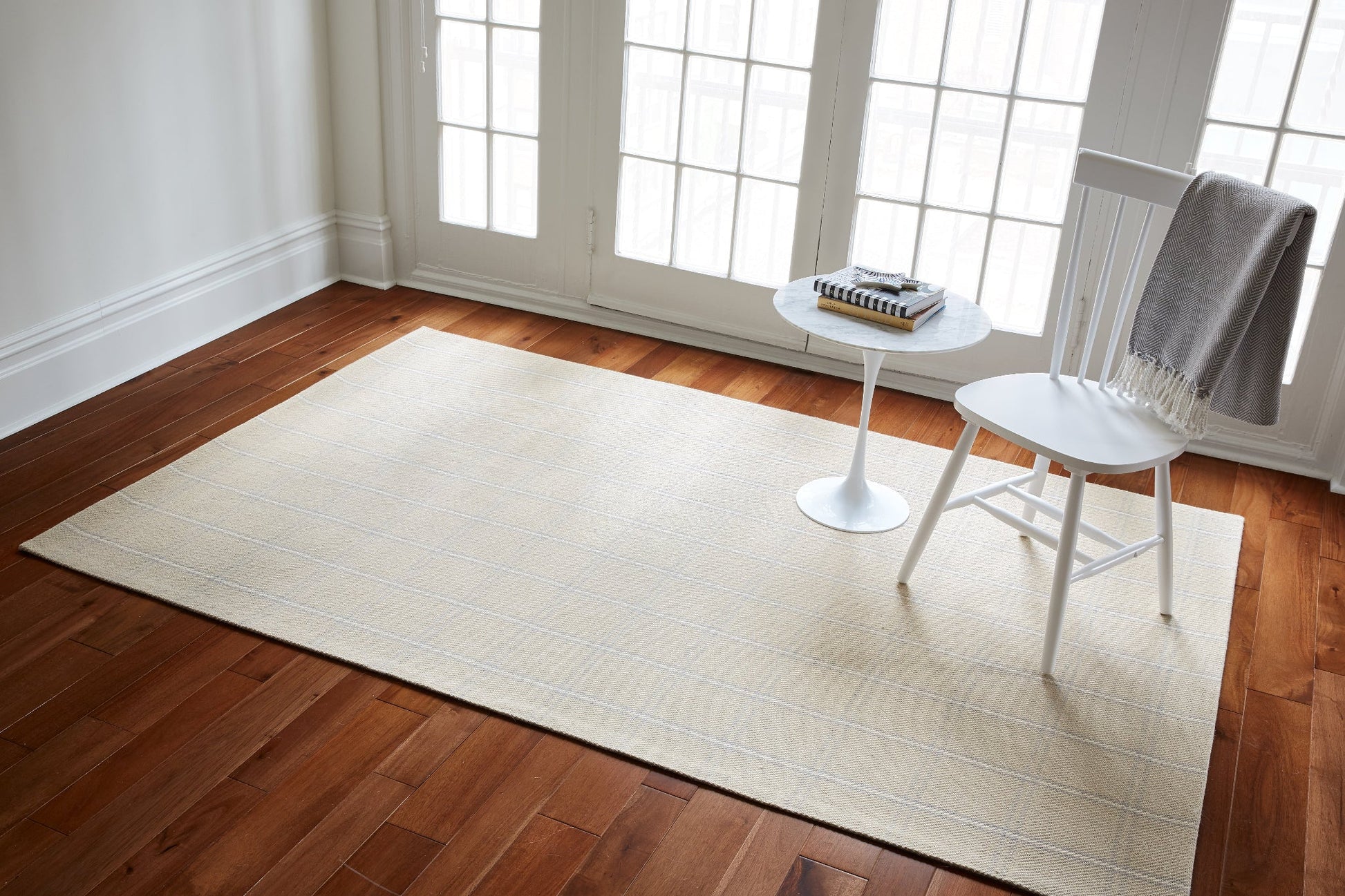 Beige striped rug on dark hardwood with white chair, gray throw, and round marble-top side table.