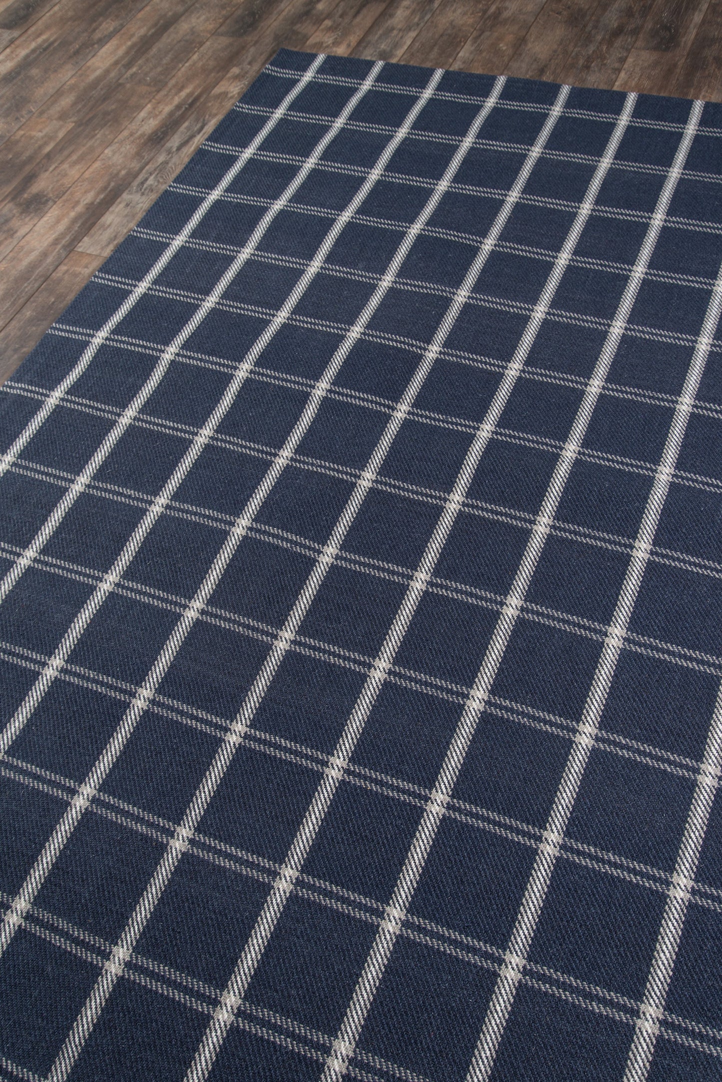 Rectangular navy rug with white grid plaid pattern on wood floor.