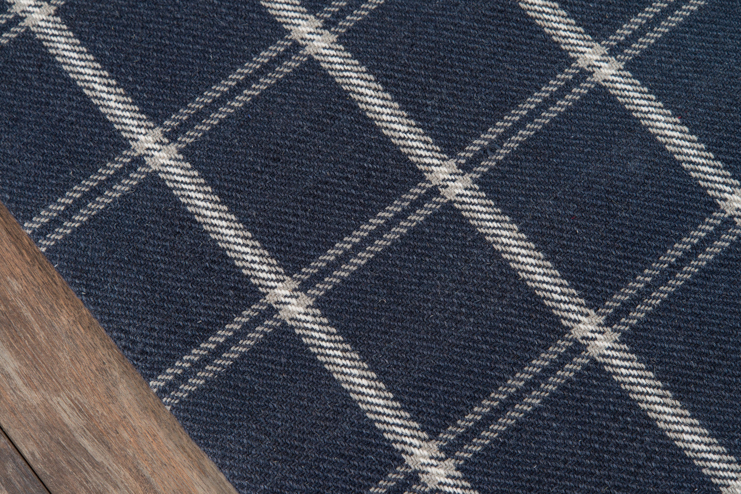Navy blue windowpane plaid wool rug with cream lines on a wooden floor.